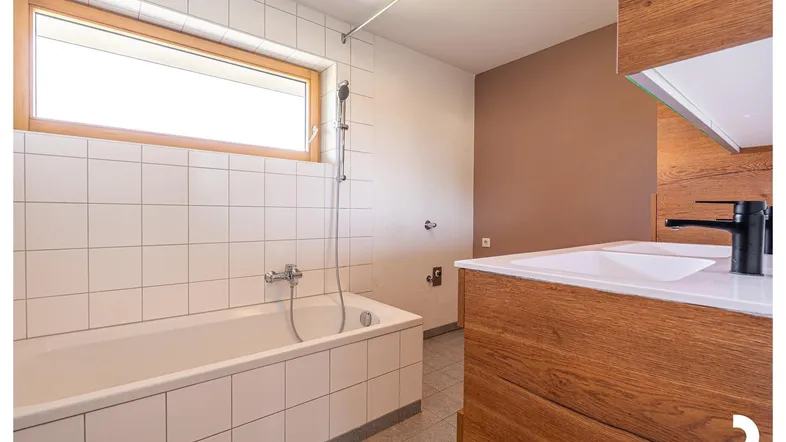 Modernes Badezimmer mit Badewanne, Holzwaschtisch und großem Fenster für natürliches Licht.