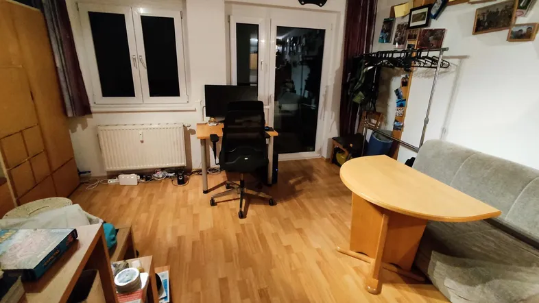 Gemütliches Wohnzimmer mit Holzboden, Schreibtisch und Zugang zu einem Balkon.