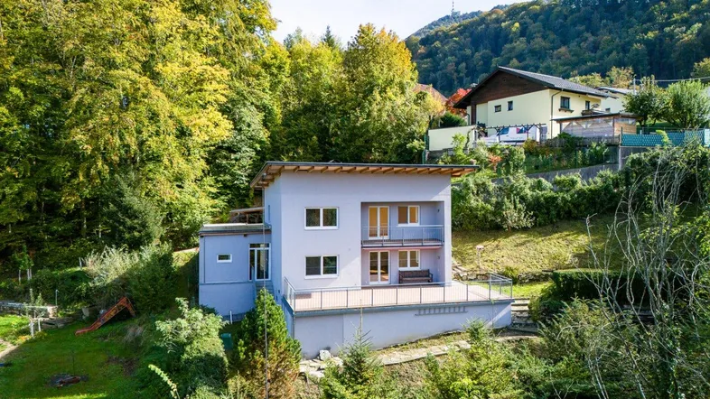 Modernes Haus mit mehreren Balkonen und einer großen Terrasse, umgeben von viel Grün.