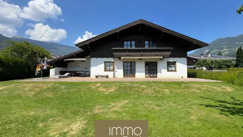 Traditionelles Haus im Alpenstil mit großem Garten und Bergblick unter blauem Himmel.