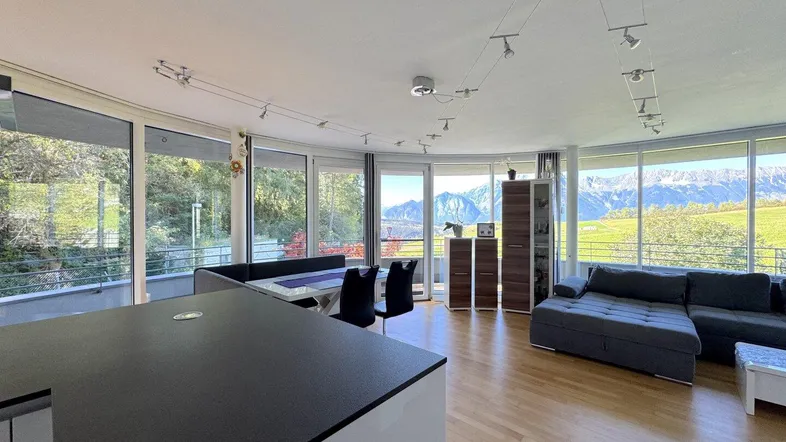 Heller offener Wohn- und Essbereich mit Panoramablick auf die Berge und Zugang zum Balkon.