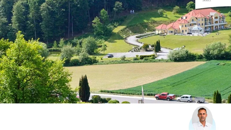 Weitläufige Ansicht eines Gebäudekomplexes inmitten von Feldern und Wäldern mit einer Zufahrtsstraße.
