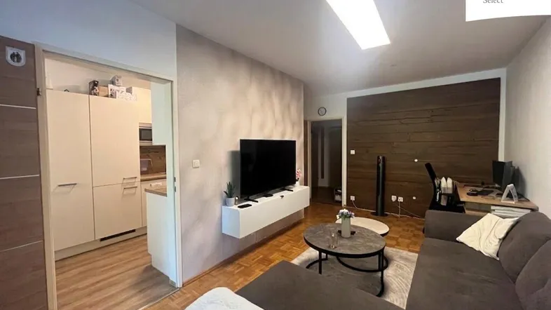 Gemütliches Wohnzimmer mit modernem TV-Möbel, Holzakzenten und Zugang zur Küche.