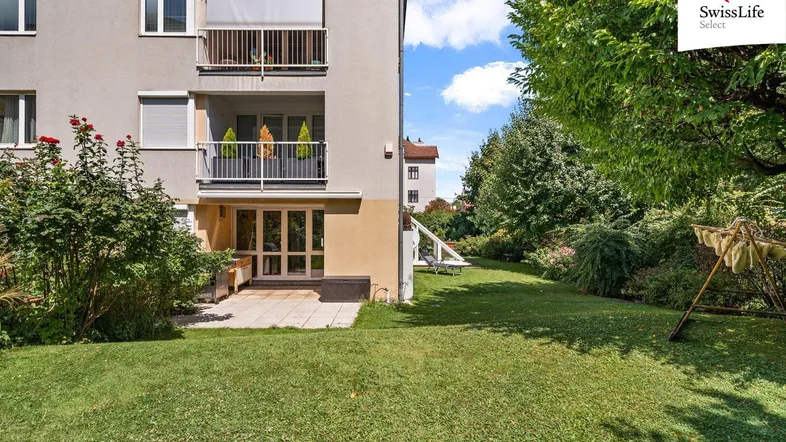 Erdgeschoss-Terrasse mit direktem Zugang zum gepflegten Garten und Blick auf die oberen Balkone des Gebäudes.