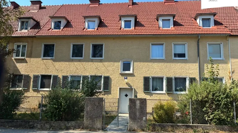 Mehrfamilienhaus mit gelber Fassade, roten Ziegeldächern und vielen Fenstern mit Fensterläden.
