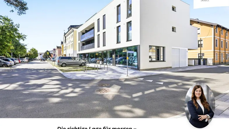 Moderne weiße Fassade eines Neubaus an einer Straße mit Parkplätzen und Geschäftsflächen.
