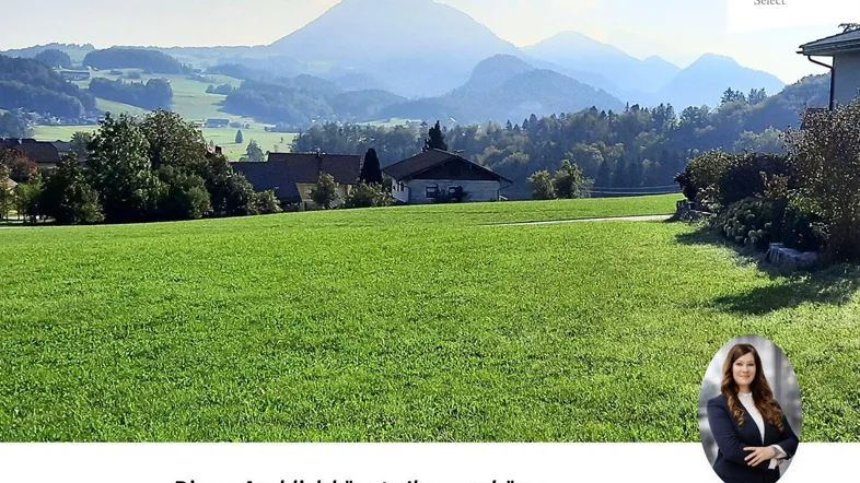 Weitläufiges grünes Feld mit majestätischem Bergblick und Häusern in der Ferne.