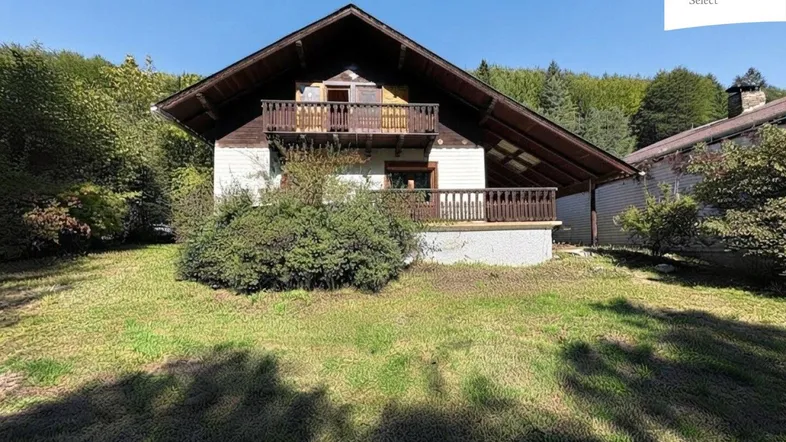 Traditionelles Haus mit Holzbalkonen und Satteldach, umgeben von viel Grün.