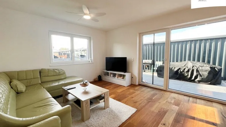 Helles Wohnzimmer mit Holzboden, bequemer Couch und Zugang zu einer Außenterrasse.