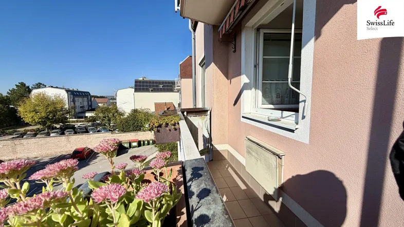 Heller Balkon mit Blumenkästen und Blick auf die Umgebung an einem sonnigen Tag.