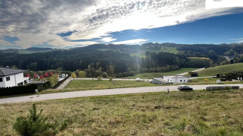 Weitläufiges Grundstück mit Blick auf sanfte Hügel und Wälder unter einem bewölkten Himmel.