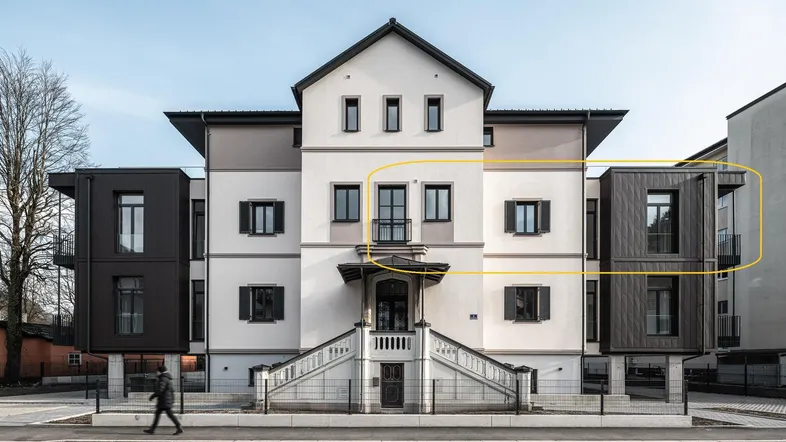 Moderne Architektur mit einer Kombination aus klassischer Fassade und dunklen, kubischen Anbauten mit großen Fenstern.