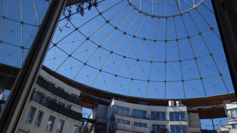 Blick nach oben in eine moderne Glaskuppel, die das Innere des Gebäudes mit Tageslicht erhellt.
