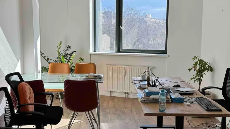 Geräumiges Büro mit mehreren Arbeitsplätzen, großen Fenstern und Holzboden, bietet viel natürliches Licht.