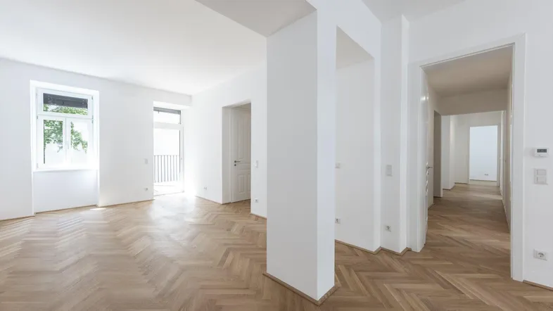 Heller, leerer Raum mit Fischgrätparkettboden und Zugang zu einem Balkon.