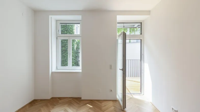 Helles Zimmer mit Fischgrätparkett und Zugang zu einem kleinen Balkon, ideal für Wohn- oder Schlafbereich.