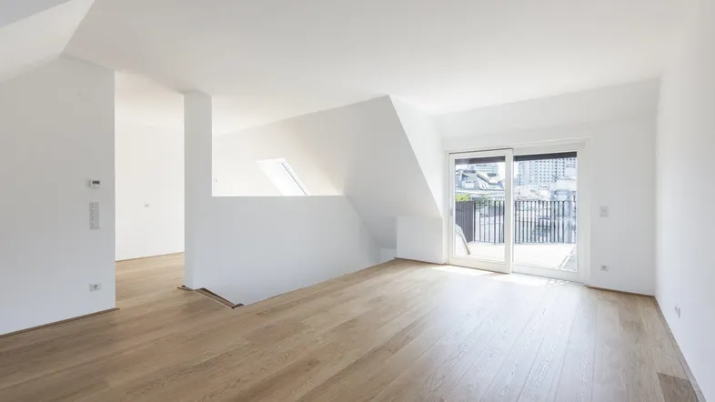 Helles, offenes Dachgeschosszimmer mit Holzboden und Zugang zu einem Balkon, ideal als Wohnbereich.