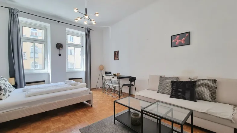 Helles Studio-Apartment mit Parkettboden, Schlaf- und Wohnbereich sowie einem kleinen Esstisch.