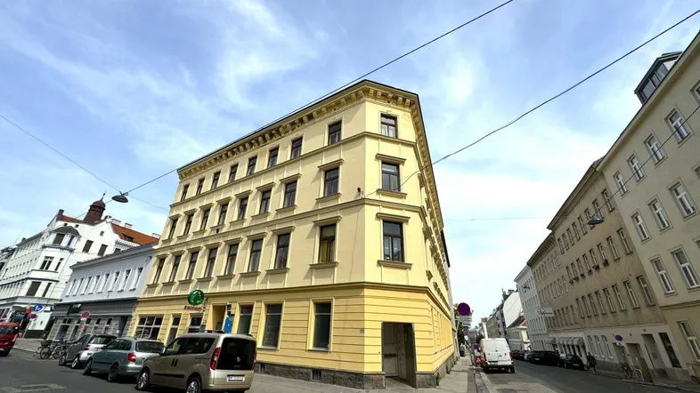 Gelbes Eckgebäude an einer Straße mit mehreren Stockwerken und vielen Fenstern.
