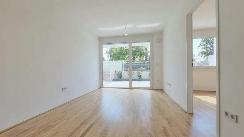 Helles, leeres Zimmer mit Parkettboden und großen Schiebetüren zu einer Terrasse.