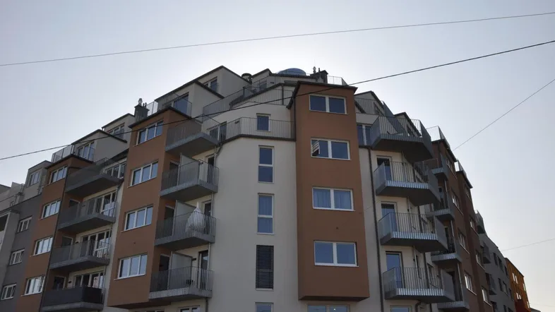 Modernes Mehrfamilienhaus mit vielen Balkonen und gestufter Dacharchitektur unter klarem Himmel.