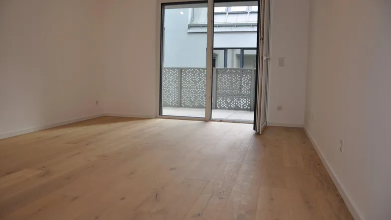 Helles Zimmer mit Holzboden und Zugang zu einem Balkon, ideal als Wohn- oder Schlafbereich.