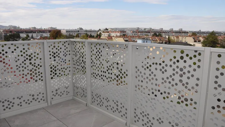 Geräumige Terrasse mit modernem Lochblechgeländer und Blick auf die umliegende Stadtbebauung.