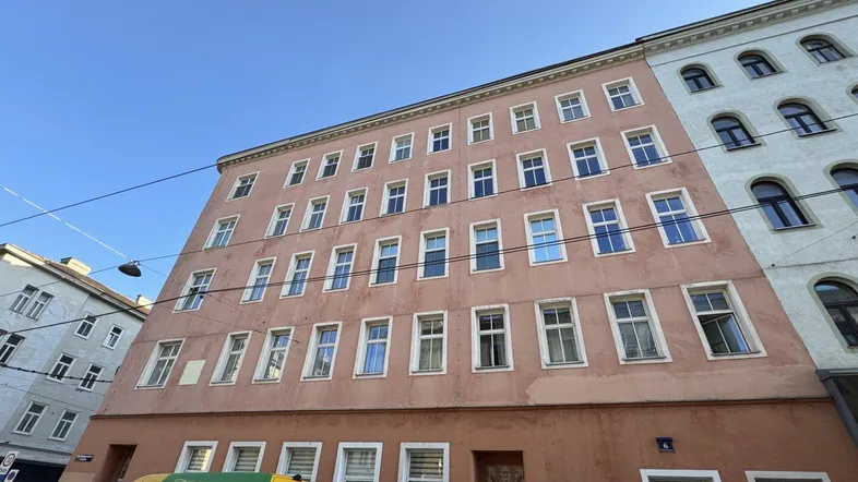 Altes Wohngebäude mit rötlich-brauner Fassade, vielen Fenstern und Rollläden in städtischer Umgebung.