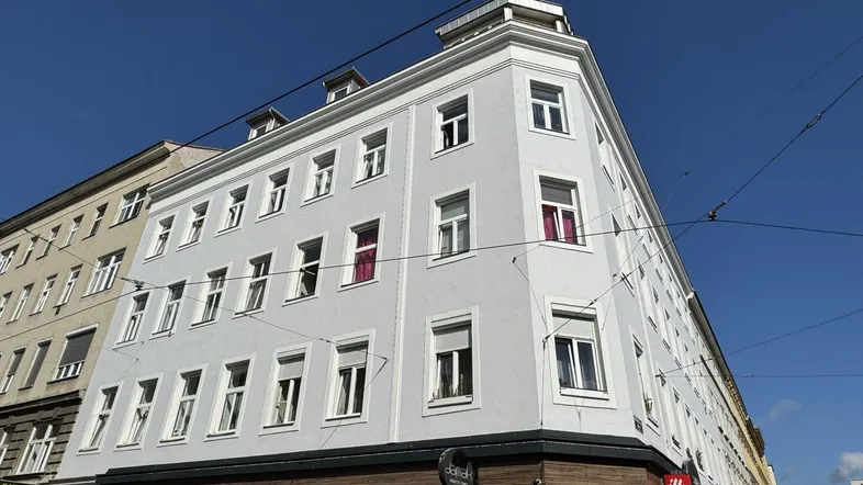 Helles Eckgebäude in der Stadt mit gepflegter weißer Fassade unter blauem Himmel.