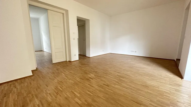 Heller, leerer Wohnraum mit Parkettboden und weißen Wänden, bereit zur individuellen Gestaltung.