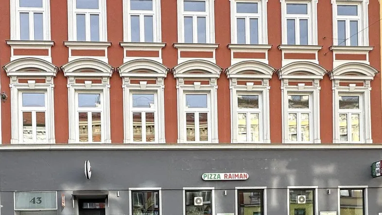 Historische rote Fassade eines Gebäudes mit vielen Fenstern und einem Geschäft im Erdgeschoss.