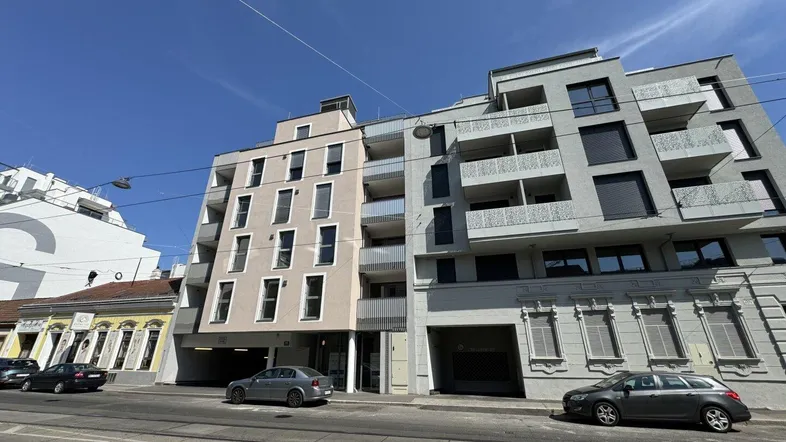 Moderne Wohngebäude-Fassade mit Balkonen und großen Fenstern an einer Stadtstraße.
