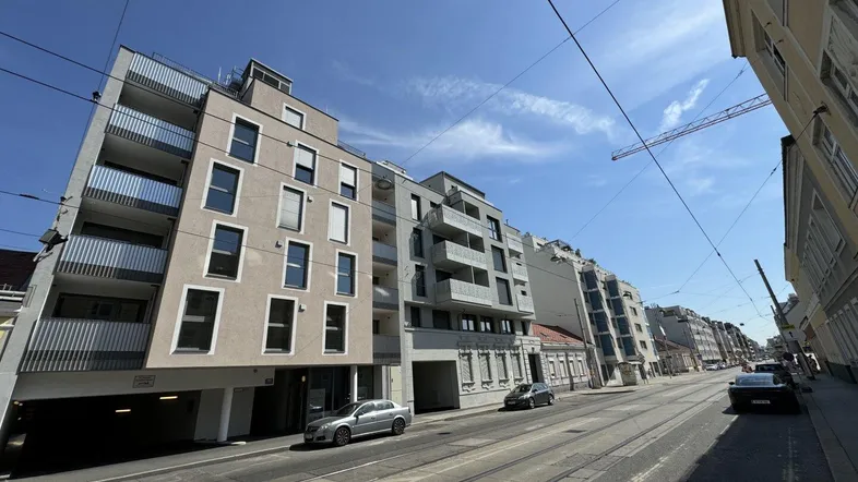 Moderne Wohngebäude an einer belebten Straße unter blauem Himmel mit Sonnenschein.