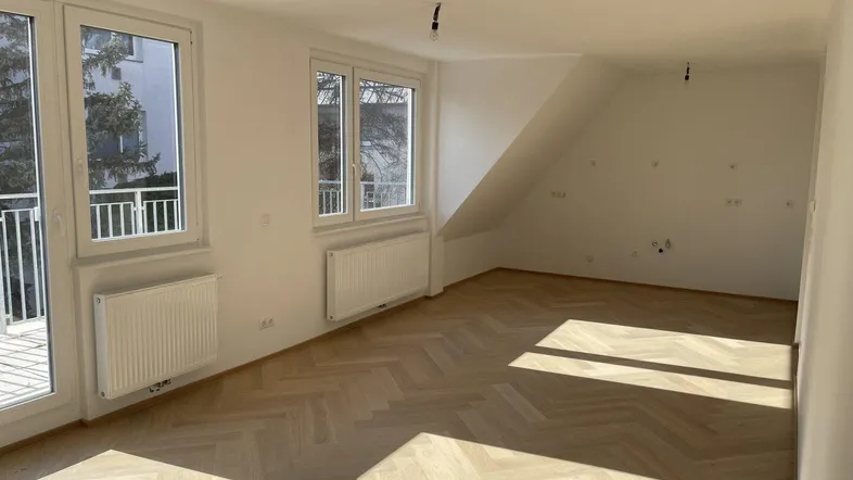 Helles Zimmer mit Fischgrätparkett, Dachschräge und Zugang zu einem Balkon.
