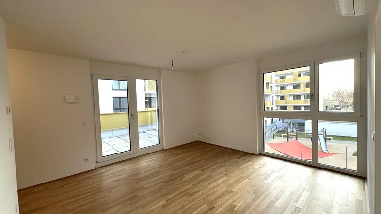 Helles Wohnzimmer mit Holzboden, großen Fenstern und Zugang zu einer Terrasse mit Blick auf einen Spielplatz.
