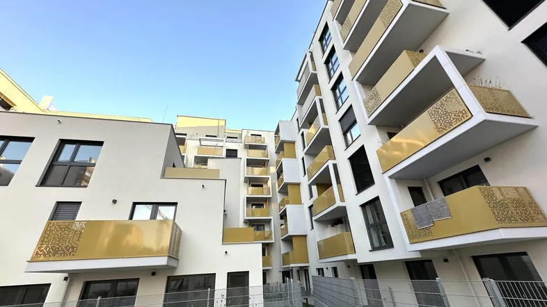 Moderne Wohngebäude mit vielen Balkonen und goldfarbenen Geländern unter klarem Himmel.