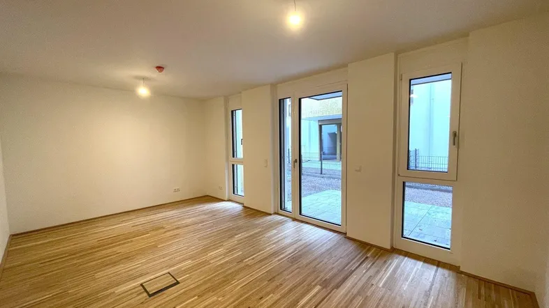 Helles, leeres Wohnzimmer mit Parkettboden und Zugang zu einem Außenbereich.
