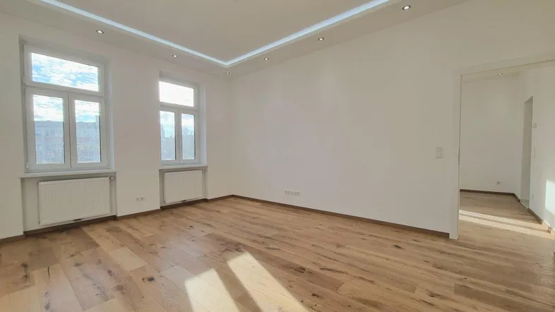 Helles, leeres Zimmer mit Parkettboden, hohen Decken und Einbaustrahlern, bereit zur individuellen Gestaltung.