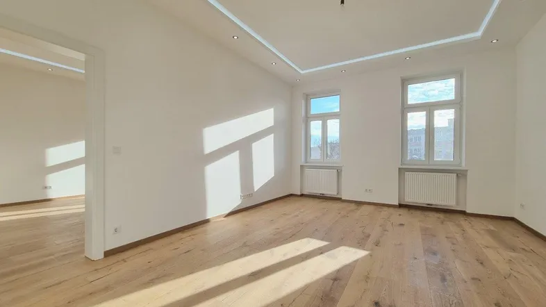 Helles, leeres Zimmer mit modernem Parkettboden, weißen Wänden und indirekter Deckenbeleuchtung.