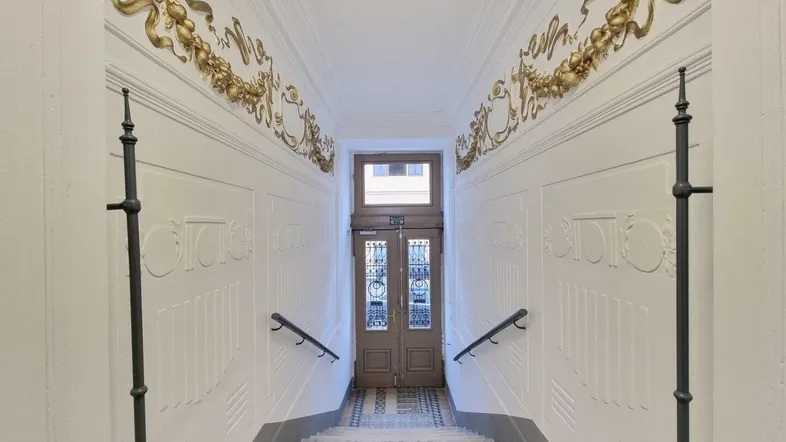 Elegantes Treppenhaus mit aufwendigen goldenen Stuckverzierungen und einer verzierten Eingangstür.