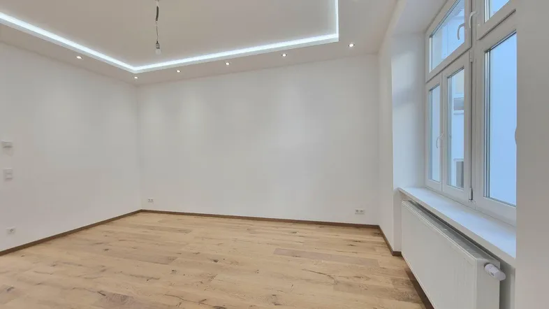 Helles Zimmer mit modernem Parkettboden, weißen Wänden und integrierter Deckenbeleuchtung.