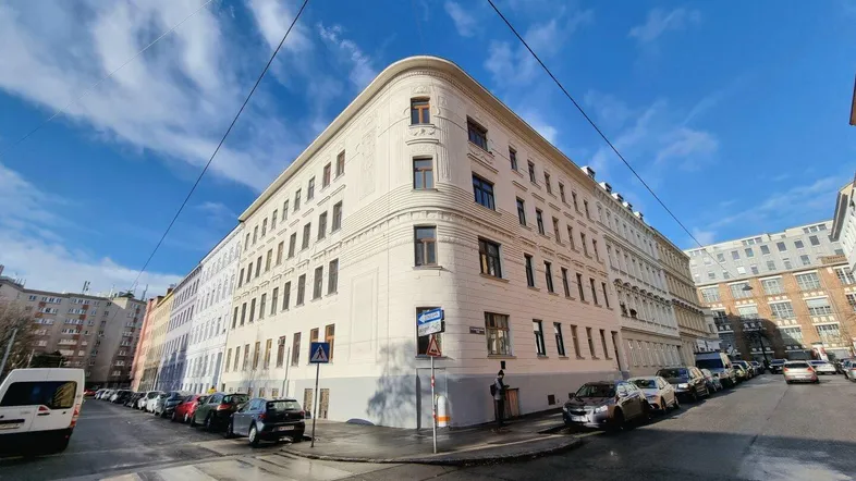 Außenansicht eines Eckgebäudes mit klassischer Architektur und vielen Fenstern unter blauem Himmel.
