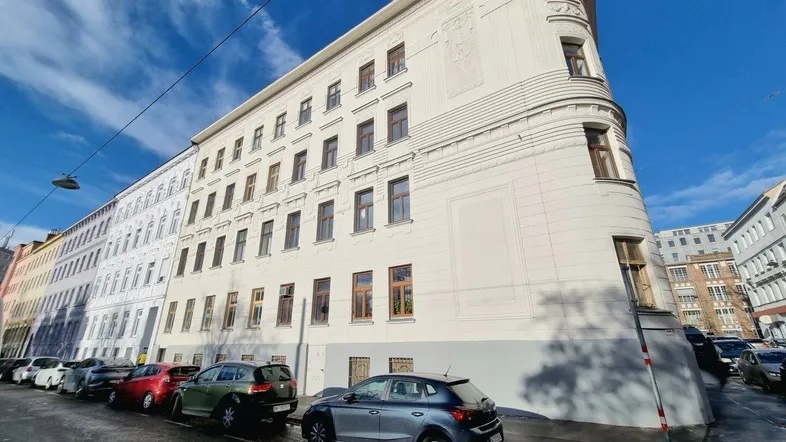 Gebäude an einer Straßenecke mit klassischer Architektur und vielen Fenstern unter blauem Himmel.