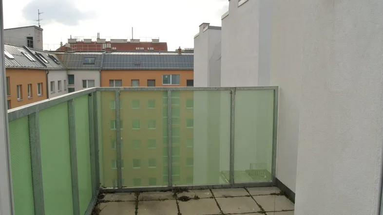 Balkon mit Blick auf umliegende Gebäude und grüner Glasbrüstung.