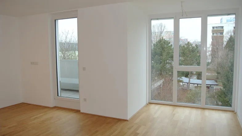Helles Zimmer mit großen Fenstern, Holzboden und Zugang zu einem kleinen Balkon.