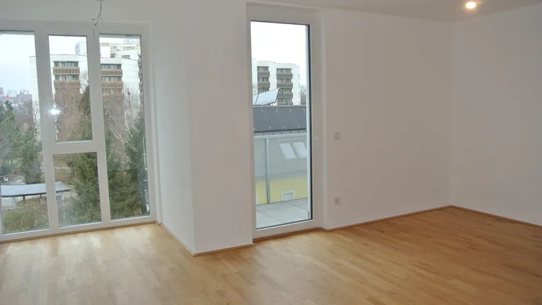 Heller Raum mit Parkettboden, großen Fenstern und Zugang zu einem Außenbereich, bietet viel natürliches Licht.