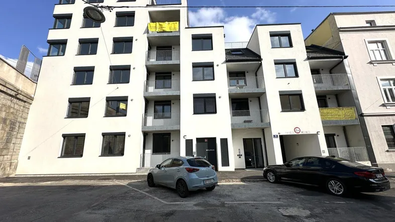 Modernes Mehrfamilienhaus mit weißer Fassade, Balkonen und großen Fenstern in städtischer Umgebung.