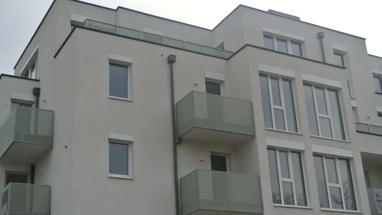 Moderne Fassade eines Mehrfamilienhauses mit mehreren Balkonen und großen Fenstern.