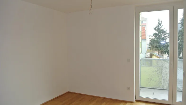 Heller Raum mit weißen Wänden und Holzboden, der Zugang zu einem Balkon bietet.