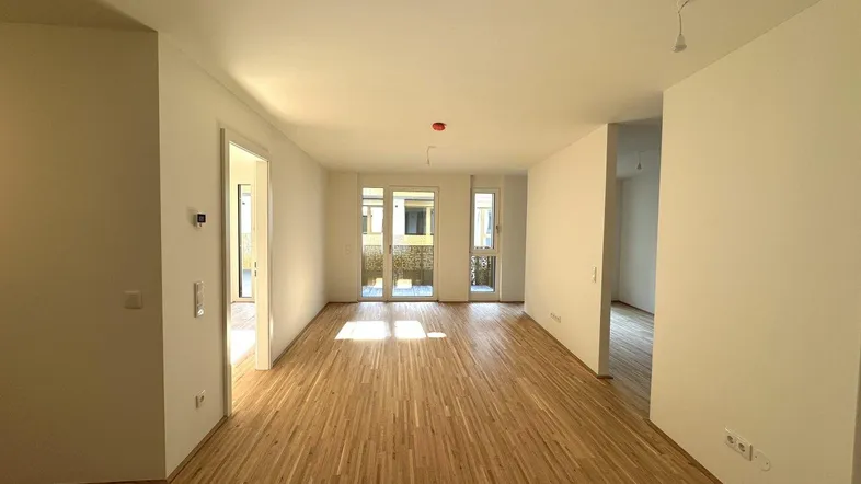 Helles, leeres Wohnzimmer mit Parkettboden und Zugang zu einem Balkon, bereit zum Einzug.